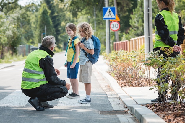 Foto un policía agachado delante de un peatón explica a un grupo de escolares cómo cruzar la calle