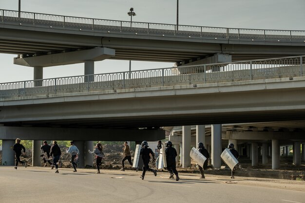 Foto la policía antidisturbios con escudos corriendo por los jóvenes infractores debajo de los puentes para atraparlos y arrestarlos.