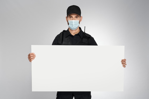 Policial bonito usando máscara protetora segurando banner em branco no estúdio