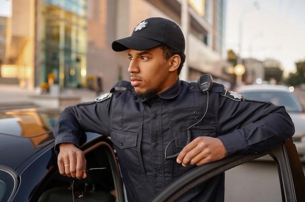 Policial de uniforme posa para o carro patrulha