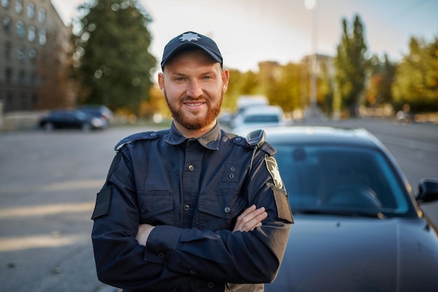 Policial masculino em uniforme posa perto do carro