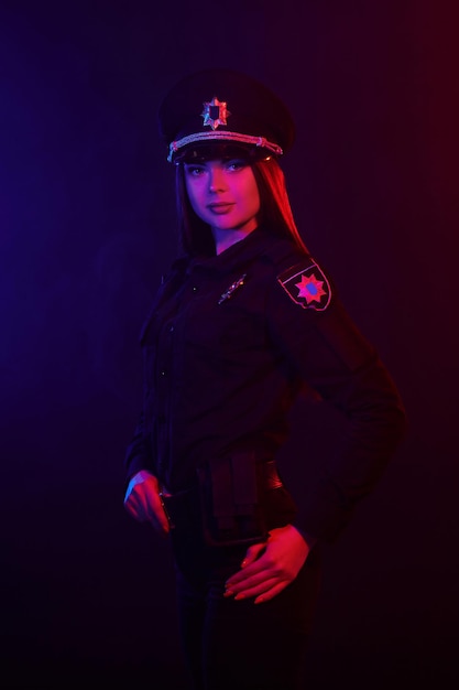 Policial ruiva posando para a câmera em um fundo preto com vermelho e azul.