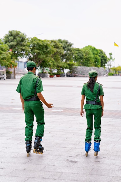 Policías con uniforme verde patinando en la plaza Ho Chi Minh en la ciudad vieja de Vietnam en Asia. Policía hombre y mujer en patines en el parque. Oficiales de seguridad en el trabajo.