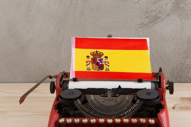 Foto politische nachrichten und bildungskonzept rote schreibmaschinenflagge spaniens auf tisch auf grauem hintergrund