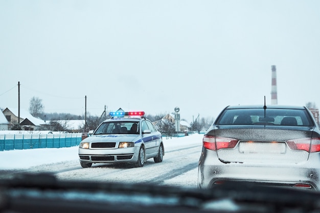 Polizeiwagen mit den roten und blauen Blitzlichtern stoppte Auto auf schneebedeckter Straße des Winters