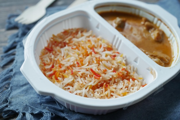 Pollo al curry y arroz en un paquete de plástico para llevar en la mesa