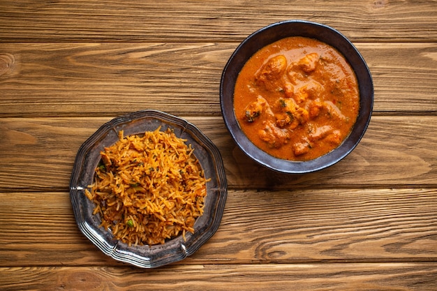 Pollo al curry indio en tazón de fuente de metal antiguo y pilaf con arroz biryani sobre fondo rústico de madera. Plato tradicional indio con mantequilla de pollo tikka masala y pilaf, almuerzo o cena saludable. Vista superior