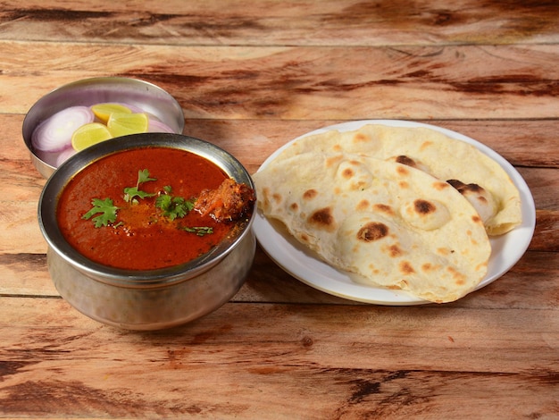 Pollo al curry Masala con una pierna prominente con pan plano indio Tava Roti servido sobre una mesa rústica de madera con enfoque selectivo