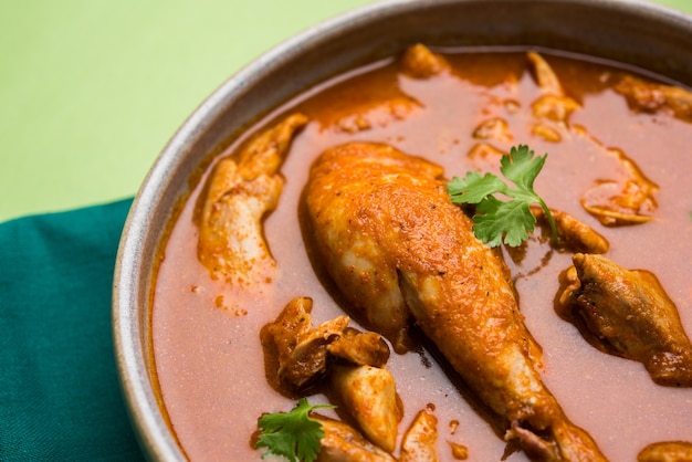 Pollo al curry rojizo picante o Masala, con un trozo de pierna prominente, servido en un cuenco o Kadhai sobre un fondo colorido o de madera. enfoque selectivo.