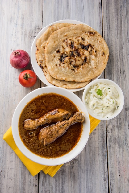 Pollo al curry rojizo popular o Masala, con pierna prominente, servido en un bol con arroz pilau, chapati o roti y ensalada