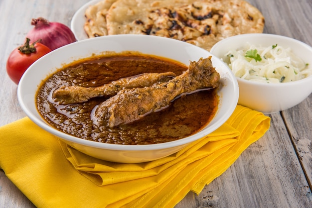 Foto pollo al curry rojizo popular o masala, con pierna prominente, servido en un bol con arroz pilau, chapati o roti y ensalada