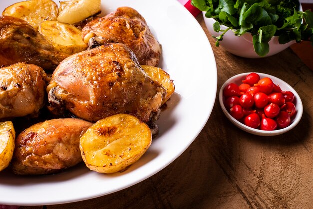 Pollo al horno en trozos con patatas y cebolla sobre un plato blanco.