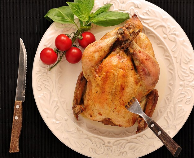 Pollo asado entero en un plato con tomate y albahaca