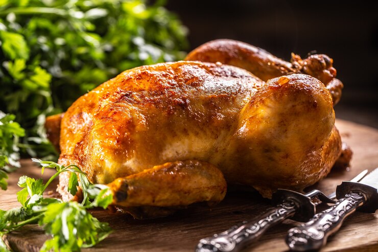 Pollo asado entero sobre una tabla de cortar de madera.