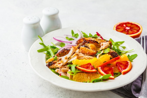 Pollo asado a la parrilla y ensalada anaranjada con la cebolla en la placa blanca en un fondo blanco.