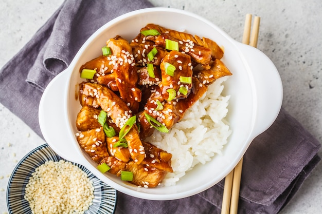 Pollo asiático del teriyaki con arroz, sésamo y cebollas verdes en el cuenco blanco.