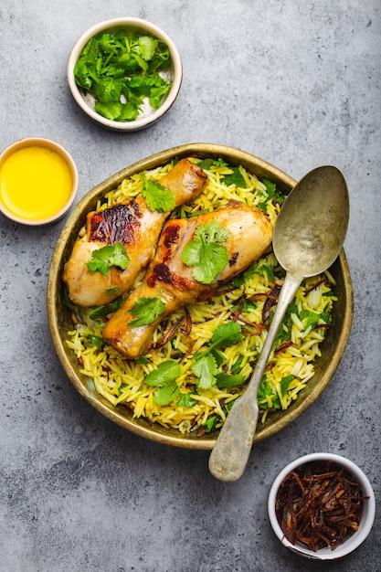 Pollo Biryani, plato tradicional de la cocina india, con arroz basmati, cebolla frita, cilantro fresco en un tazón sobre fondo de piedra rústica gris. Auténtica comida india, vista superior, primer plano