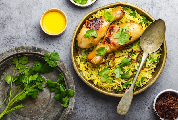 Pollo Biryani, plato tradicional de la cocina india, con arroz basmati, cebolla frita, cilantro fresco en un tazón sobre fondo de piedra rústica gris. Auténtica comida india, vista superior, primer plano