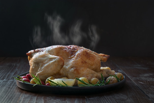 Pollo caliente asado con patatas y romero en la mesa de madera.