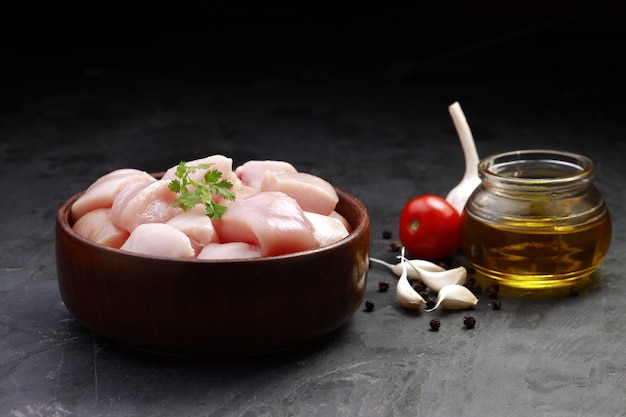 Pollo crudo biriyani cortado sin piel dispuestas en recipiente negro sobre fondo de textura de piedra