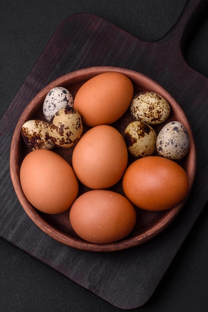 Pollo crudo y huevos de codorniz en un cuenco de cerámica marrón sobre un fondo de hormigón oscuro