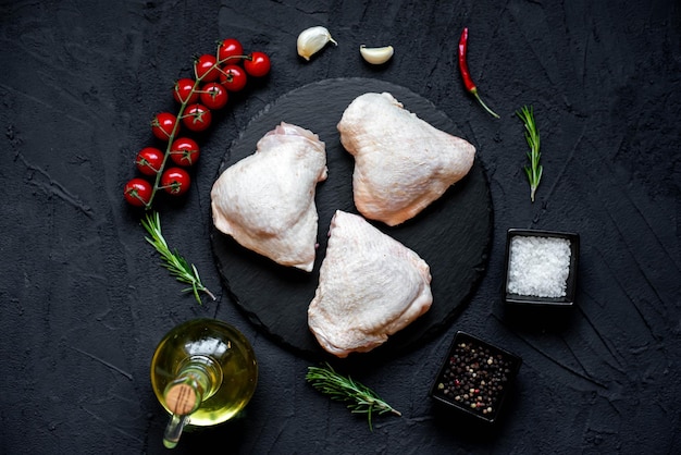 Pollo crudo sobre un fondo negro con ingredientes para cocinar.