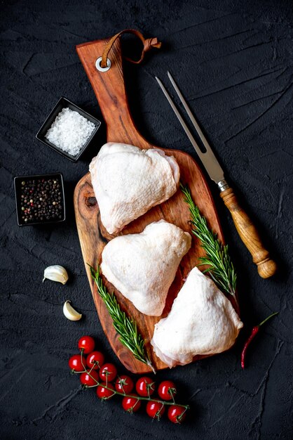 Pollo crudo sobre una tabla de madera con especias y hierbas.