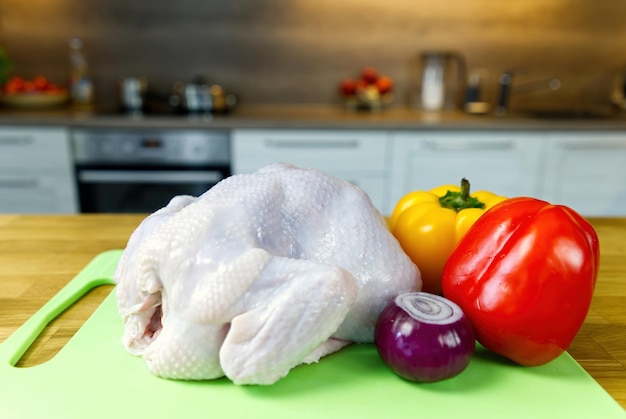 Pollo crudo en una tabla para cortar al lado de las verduras