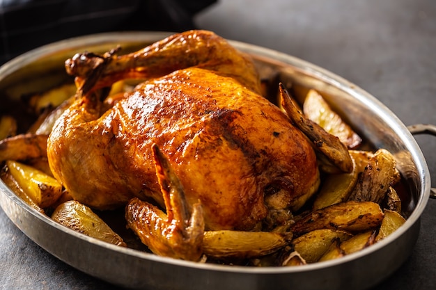 Pollo crujiente dorado entero al horno en una sartén cocido con patatas.