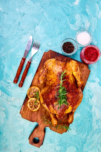 Foto pollo entero al horno con salsas en el tablero de madera sobre fondo azul.