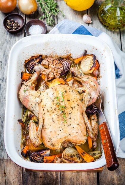 Pollo entero al horno con verduras y tomillo sobre mesa de madera