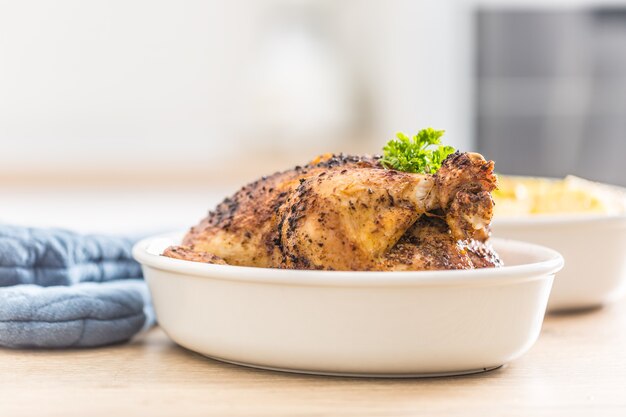 Pollo entero asado en cuenco de porcelana con patatas.