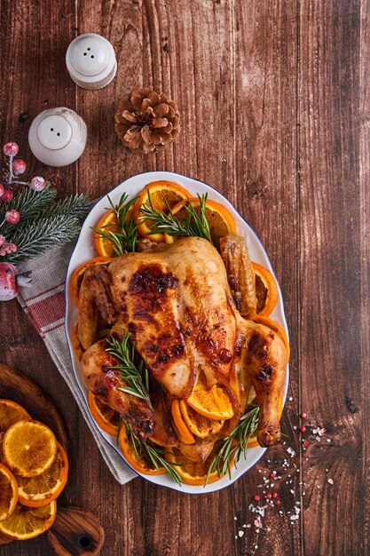 Pollo entero asado o al horno con romero y naranjas, hecho en casa para una cena familiar sobre una mesa de piedra marrón. Vista superior con espacio de copia.