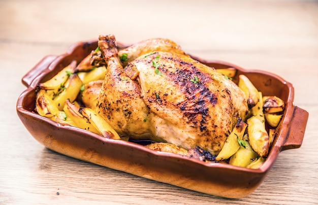 Pollo entero asado con patatas en una fuente para horno. Comida sabrosa en casa en la encimera de la cocina.