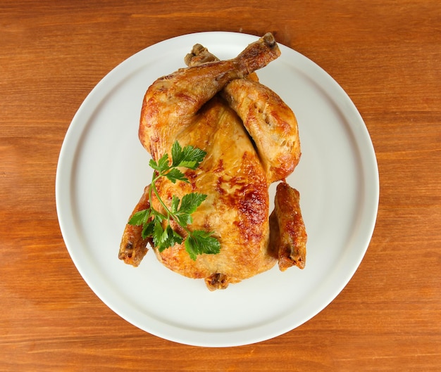 Pollo entero asado en un plato blanco sobre fondo de madera