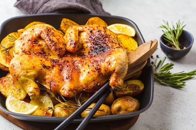 Pollo entero frito del tabaka con las patatas en una cacerola de la parrilla, visión superior, fondo blanco.