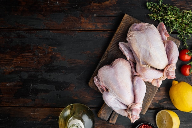 Pollo entero joven pequeño crudo con ingredientes, sobre la mesa de madera antigua, vista superior