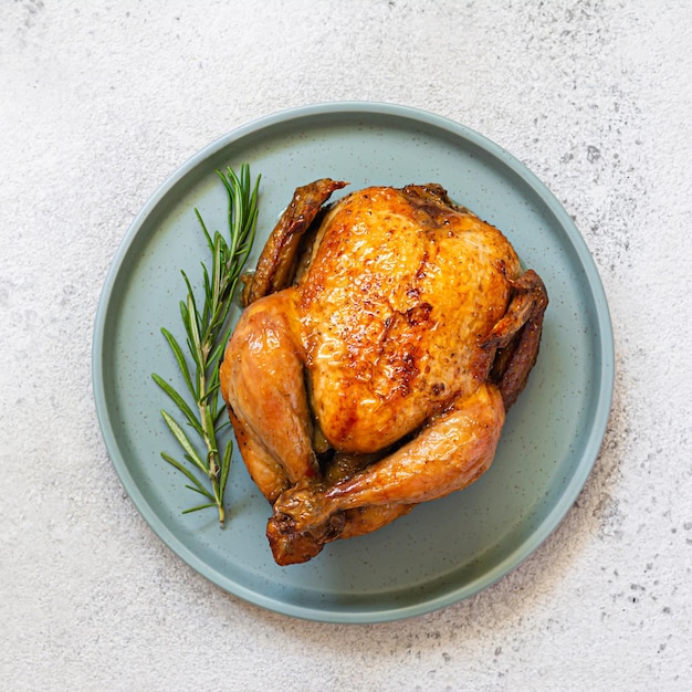 Pollo frito entero al horno con especias y romero en un plato de fondo claro