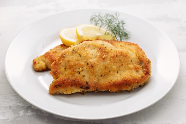 Pollo frito con limón en un plato blanco sobre fondo de cerámica