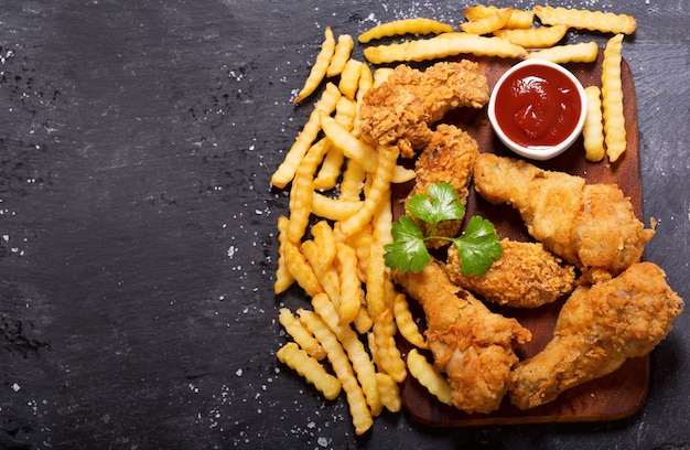 Pollo frito y papas fritas en una mesa oscura, vista superior