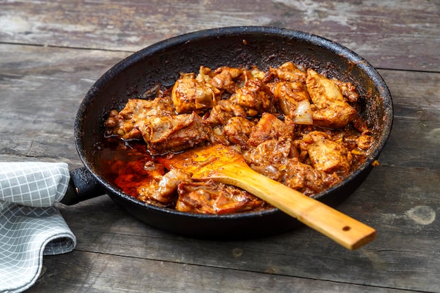 Pollo frito en una sartén con una espátula de madera sobre una mesa oscura