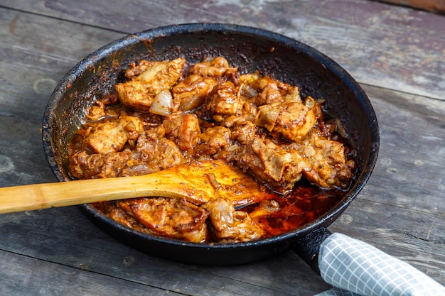 Pollo frito en una sartén con una espátula de madera sobre una mesa oscura