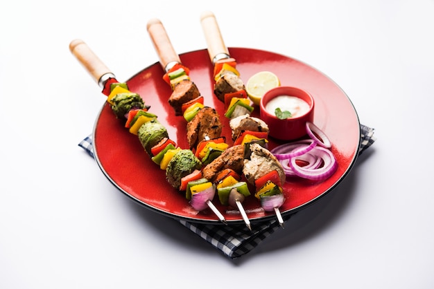 Pollo Hariyali kakab o Malai malai kebab en tricolor servido con pinchos y salsa de yogur en un plato