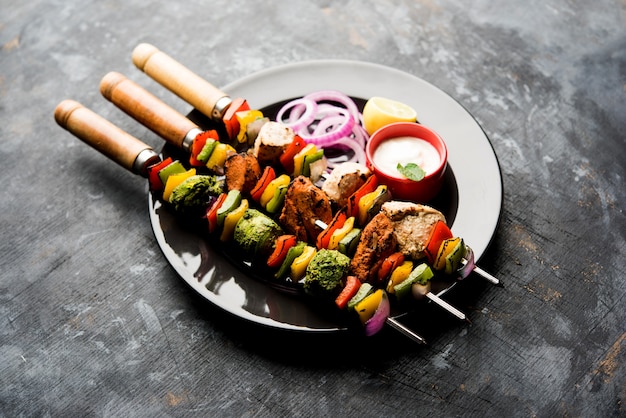 Pollo Hariyali kakab o Malai malai kebab en tricolor servido con pinchos y salsa de yogur en un plato