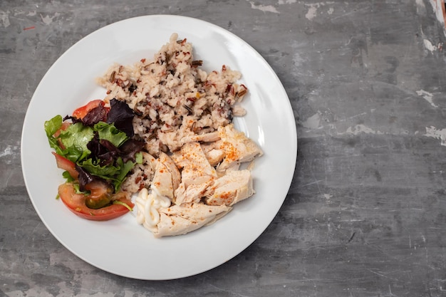 Pollo hervido con arroz y ensalada fresca en plato blanco