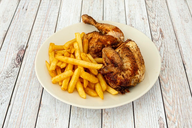 Pollo medio asado con patatas fritas en un plato blanco y una mesa de madera