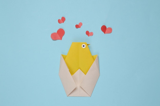 Pollo de origami y corazones sobre un fondo azul.