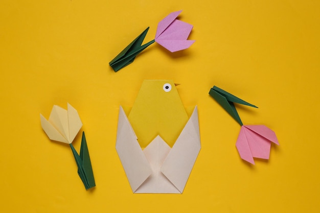 Pollo de origami y tulipanes sobre fondo amarillo Concepto de pascua de primavera