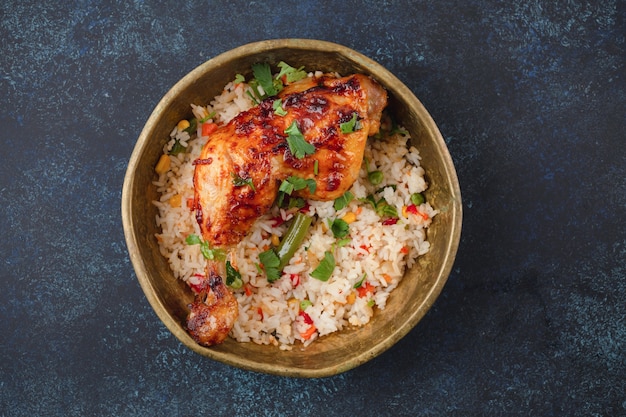 Pollo a la parrilla y arroz con verduras en placa de metal rústico en la vista superior de fondo de piedra azul. Comida de Oriente Medio o India para el almuerzo o la cena, desde arriba