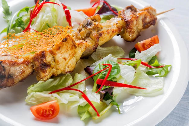 Pollo a la parrilla carne en palo con ensalada y tomates en plato blanco